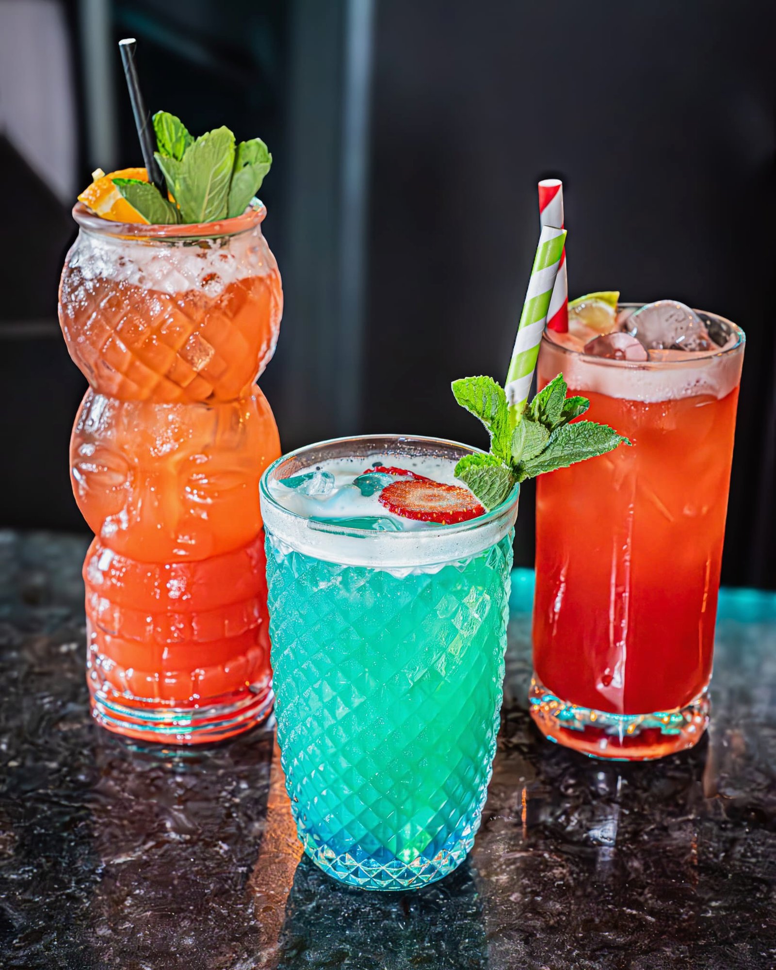 Three colourful cocktails garnished with fruit and mint